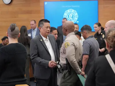Mayor Frank Aurelio Yokoyama shaking hands with a Los Angeles County Sheriff's deputy inside the City Council Chamber.